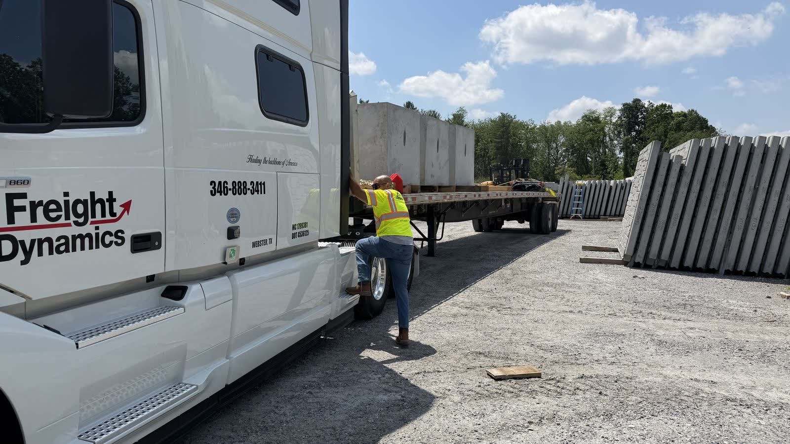 Driver boarding a Freight Dynamics Volvo, MC and DOT numbers on the cab, loaded flatbed behind